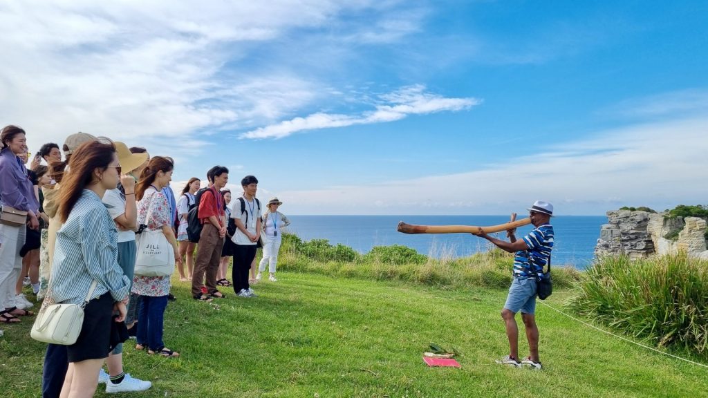 walangari playing didgeridoo for aboriginal cultural walking tour group at bondi sydney